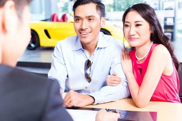 Un couple souriant signant des contrats pour un achat chez un concessionnaire automobile.