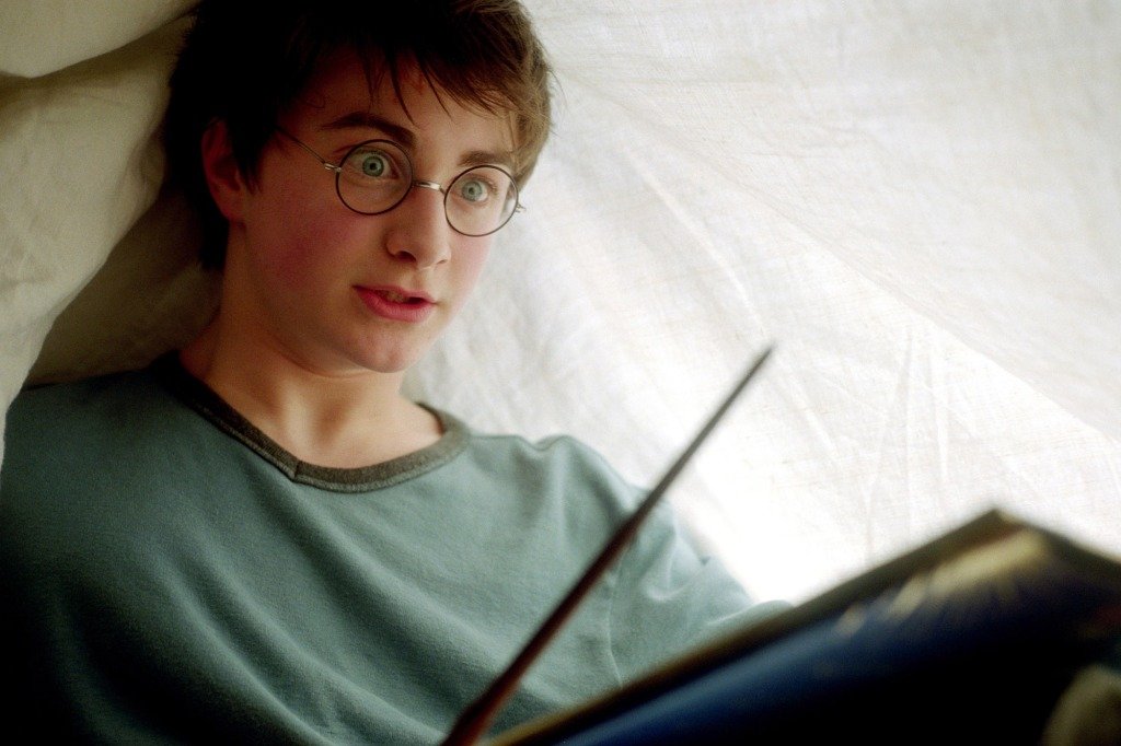 Harry Potter pratique ses sorts sous une couverture.