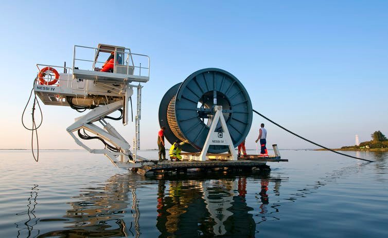 Une équipe travaille sur une machine avec une bobine géante posant un câble dans l'eau
