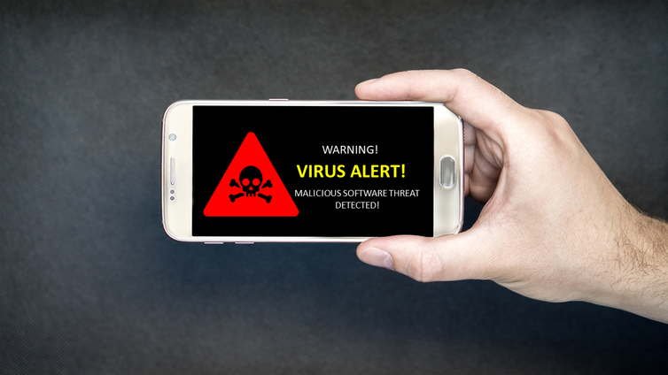 Un smartphone avec un avertissement d'alerte de virus est tenu par une main devant un fond sombre.