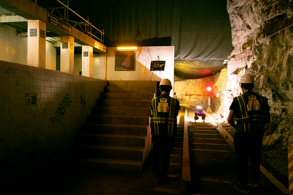A photo of a robot approaching a pair of people and near an underground train station