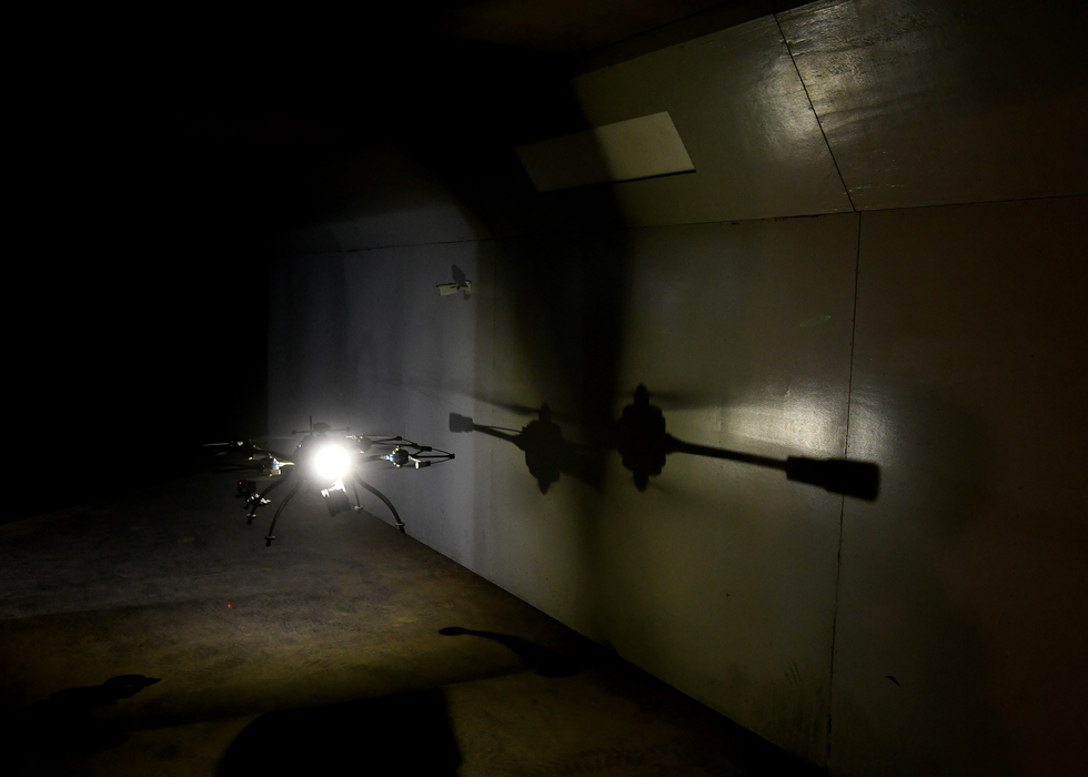 A photo of a flying drone hovering in a dark area.