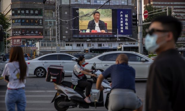 Des gens dans une rue de Pékin avec Xi Jinping sur un écran de télévision géant
