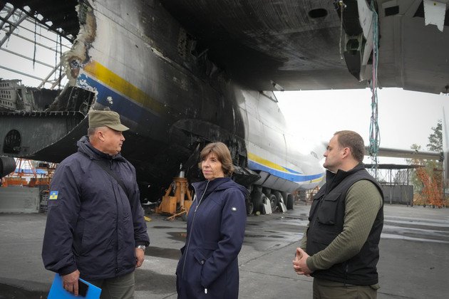 La ministre française des Affaires étrangères Catherine Colonna se tient entre deux hommes devant les ruines de l'Antonov An-224, le plus gros avion cargo du monde.