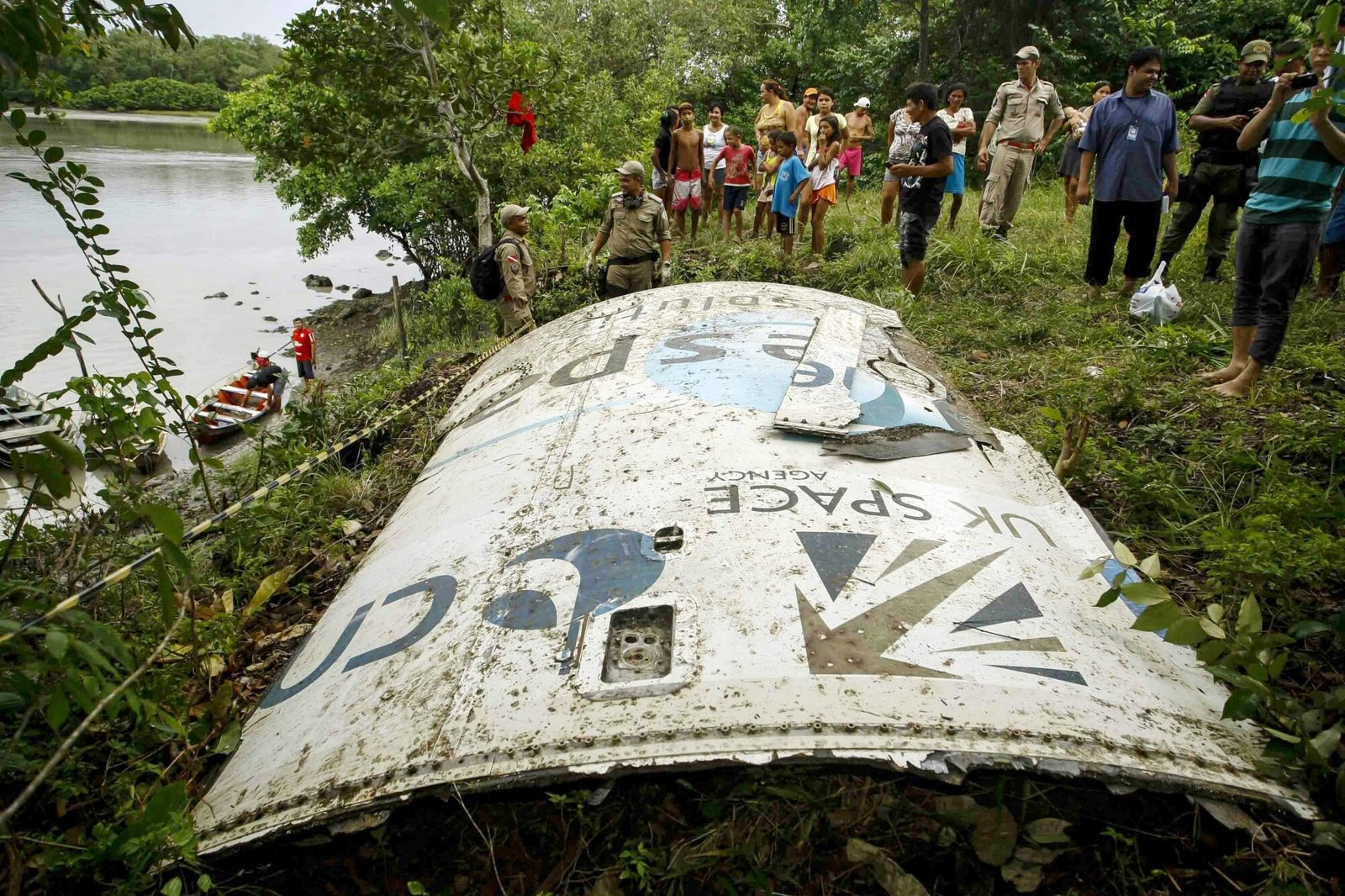 Un gros morceau blanc de débris d'un vaisseau spatial repose dans l'herbe au bord d'une rivière au Brésil. Le morceau de métal a les mots