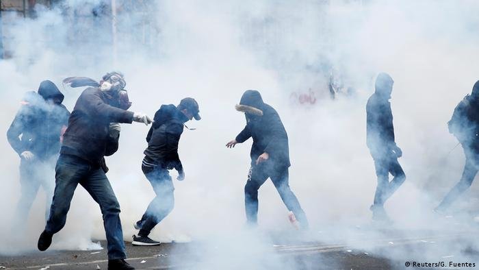 Entourés de gaz lacrymogènes, des manifestants masqués vêtus de noir lancent des objets à Paris lors d'une grève nationale. Entourés de gaz lacrymogènes, des manifestants masqués vêtus de noir lancent des objets à Paris lors d'une grève nationale.