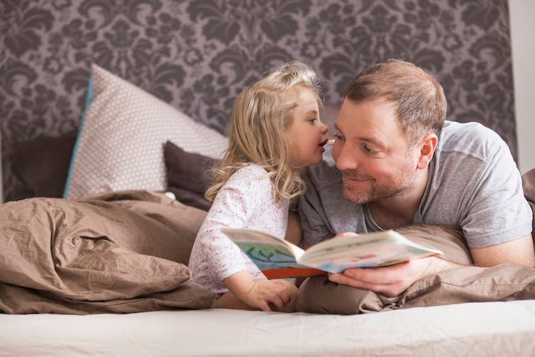 petite fille chuchote à un homme pendant qu'ils lisent sur un lit