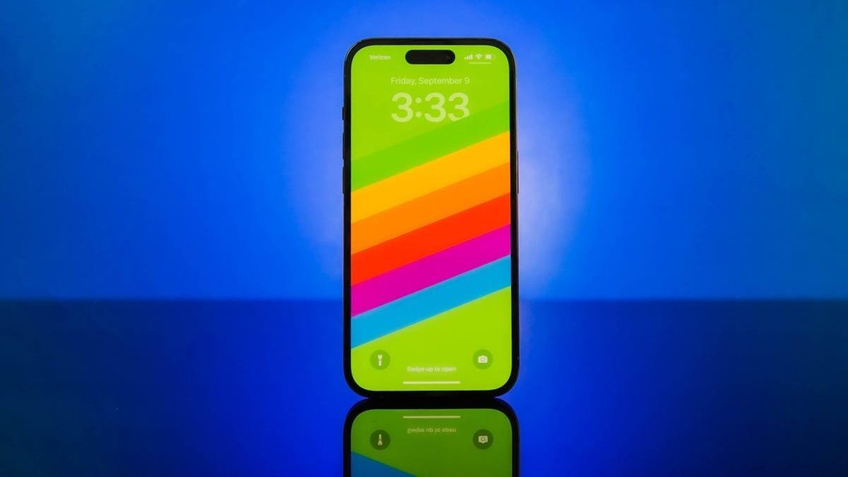 Un iPhone 14 avec un arrière-plan arc-en-ciel à l'écran sur fond bleu