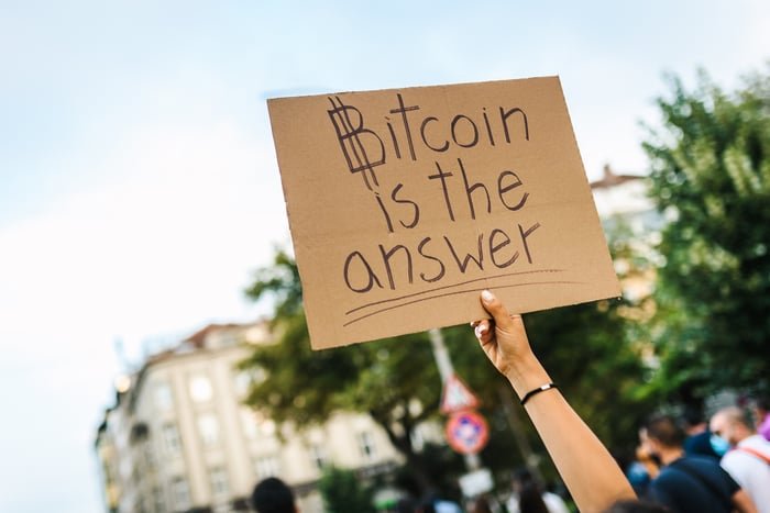Une personne brandissant une pancarte en carton indiquant que Bitcoin est la réponse.