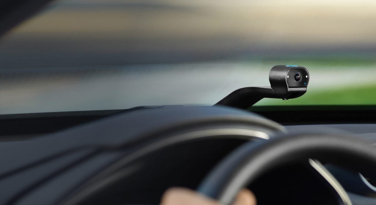 La Ring Car Cam, une dashcam à double face avec connectivité Wi-Fi, se trouve au sommet du tableau de bord d'un véhicule passant devant un arrière-plan bokeh.