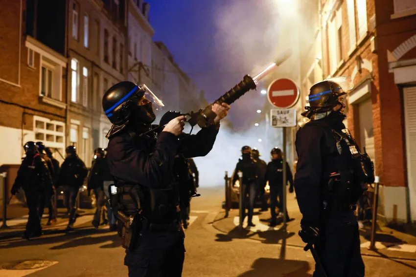 TOPSHOT - Un policier français en tenue anti-émeute tire un lanceur de gaz lacrymogène lors d'une manifestation après que le gouvernement français a poussé une réforme des retraites au Parlement sans vote, en utilisant l'article 49,3 de la constitution, à Lille, dans le nord de la France, en mars 16 mars 2023. - Le 16 mars, le président français a fait passer une réforme controversée des retraites au parlement sans vote, déployant un pouvoir constitutionnel rarement utilisé qui risque d'enflammer les protestations. Cette décision était un aveu que son gouvernement n'avait pas la majorité à l'Assemblée nationale pour adopter la législation visant à relever l'âge de la retraite de 62 à 64 ans. (Photo de Sameer Al-Doumy / AFP) (Photo de SAMEER AL-DOUMY/AFP via Getty Images)