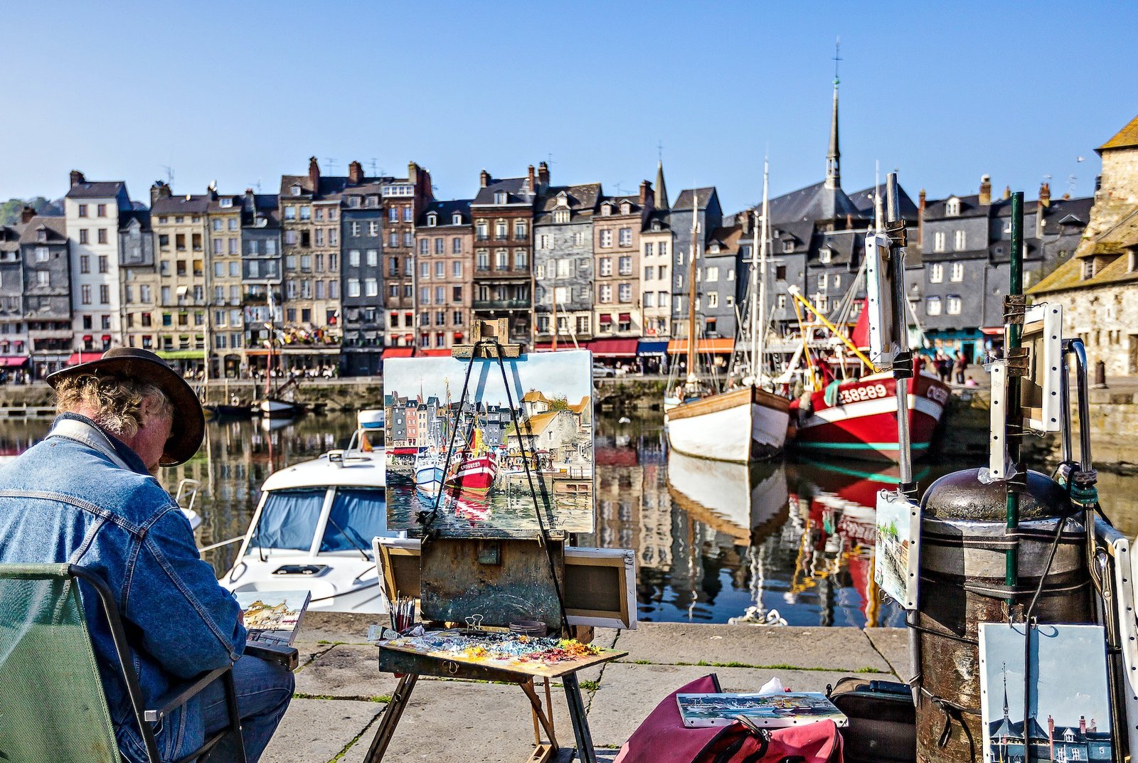 Un artiste peint sur un chevalet dans le port historique rempli de voiliers de Honfleur, Normandie, France