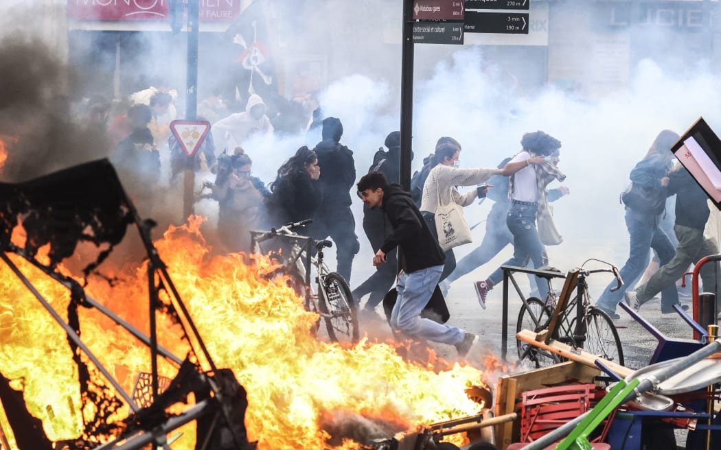 Les manifestants courent dans la fumée des gaz lacrymogènes à côté d'un incendie de rue en marge d'une manifestation dans le cadre d'une journée nationale de grèves et de manifestations, une semaine après que le gouvernement français a poussé une réforme des retraites au parlement sans vote, en utilisant l'article 49.3 de la constitution, à Toulouse, dans le sud de la France, le 23 mars 2023. - Le 23 mars, les syndicats français ont organisé une nouvelle journée de perturbations contre la réforme des retraites du président après qu'il s'est engagé avec défi à mettre en œuvre le changement, qui comprend le relèvement de l'âge de la retraite de 62 à 64, disant qu'il était prêt à accepter l'impopularité face à des protestations parfois violentes. (Photo Charly TRIBALLEAU / AFP)