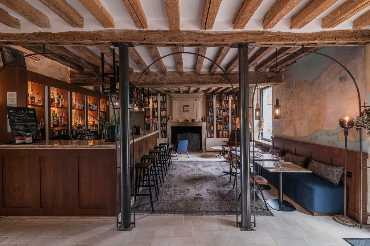 The view through several large wire frame arches into a dining room with a blue leather banquette on one side and a bar on the other, with a library visible beyond. 