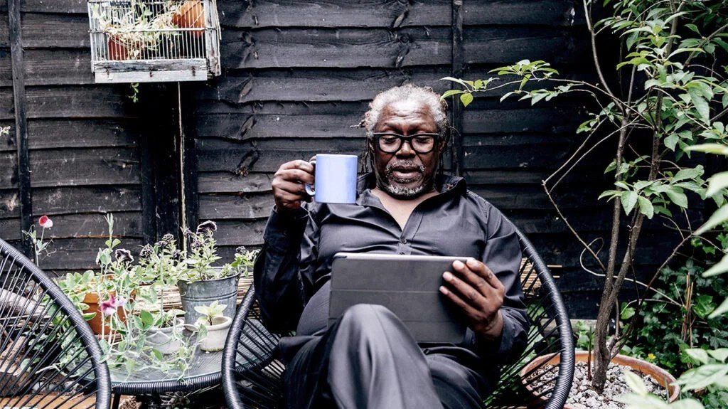 Démence : la navigation sur Internet peut aider à se protéger contre la démence 1 Un homme noir plus âgé portant des lunettes utilisant Internet et lisant une tablette tout en buvant du café sur une terrasse extérieure