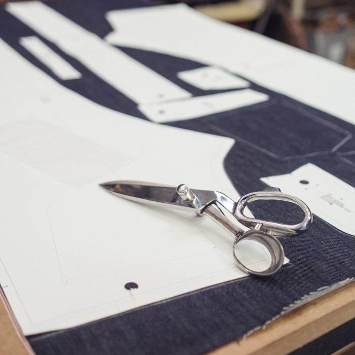 Un textile denim est disposé sur une table avec des ciseaux et un patron en papier