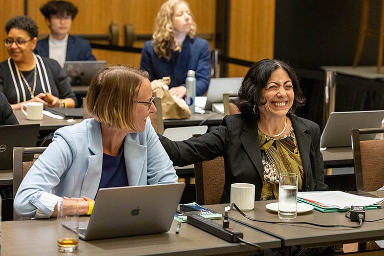 une femme portant une veste noire sourit et tapote le dos d'une femme portant un blazer bleu