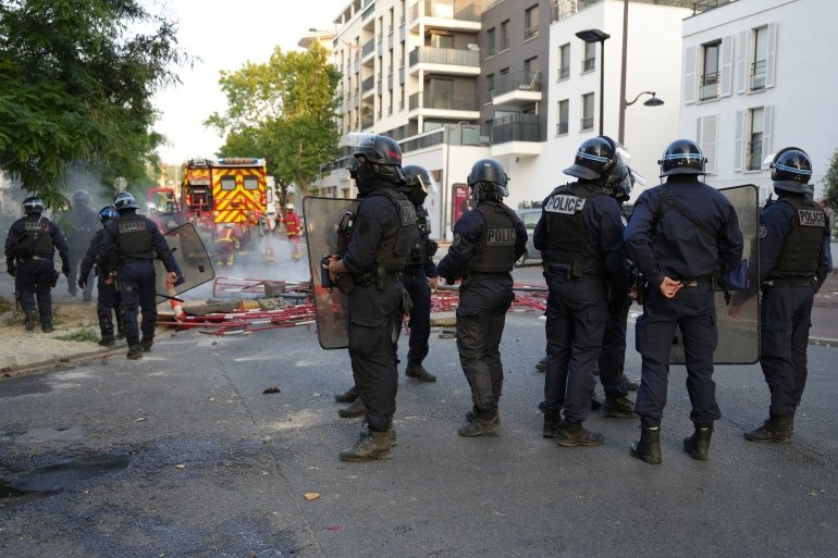 Des policiers en tenue anti-émeute montent la garde alors que les pompiers s'efforcent d'éteindre les incendies après une manifestation à Nanterre, à l'ouest de Paris, le 27 juin 2023, après que la police française a tué un adolescent qui refusait de s'arrêter pour un contrôle routier dans la ville. – Le jeune de 17 ans se trouvait dans la banlieue parisienne tôt le 27 juin lorsque la police l'a abattu après avoir enfreint le code de la route et ne s'est pas arrêté, ont déclaré les procureurs. L'événement a suscité des expressions de choc et des questions sur la volonté des forces de sécurité d'appuyer sur la gâchette. (Photo de Zakaria ABDELKAFI / AFP)