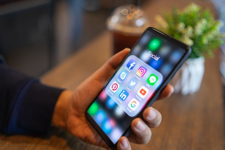 Une main tenant un téléphone portable affichant un groupe d'icônes de plate-forme de médias sociaux