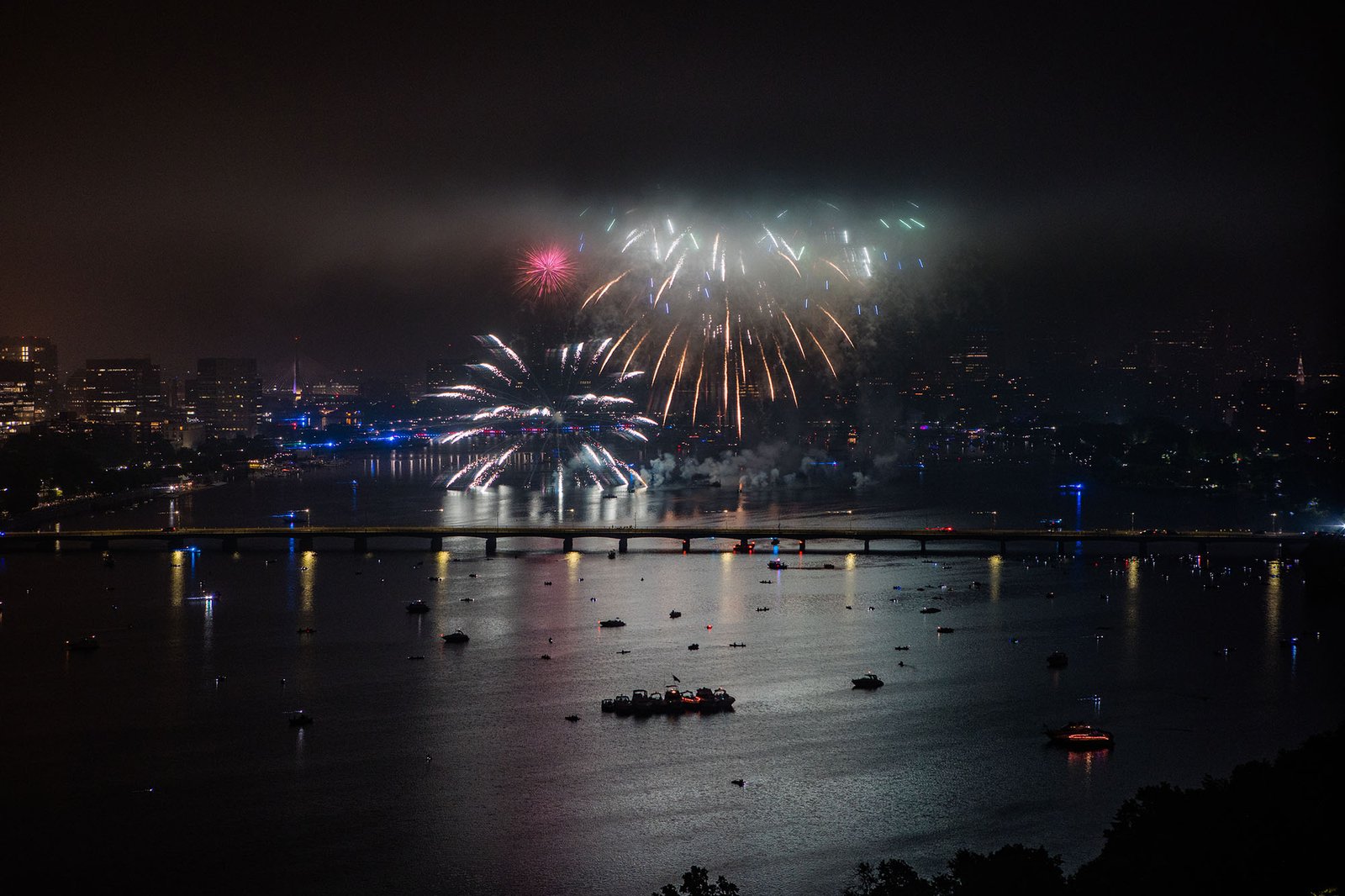 Photo : les feux d'artifice du 4 juillet se déclenchent par une nuit noire au-dessus de la rivière Charles.  Des feux d'artifice blancs et jaunes illuminent le ciel nocturne et montrent l'horizon de Boston.