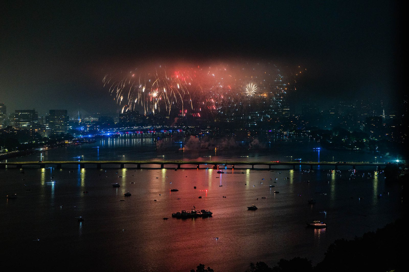 Photo : les feux d'artifice du 4 juillet se déclenchent par une nuit noire au-dessus de la rivière Charles.  Des feux d'artifice rouges, blancs et orange illuminent le ciel nocturne et montrent l'horizon de Boston.