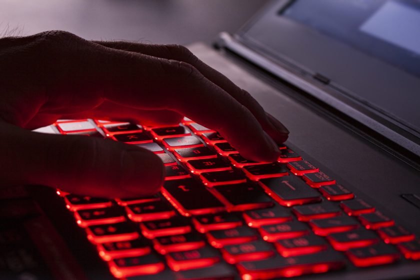 Gros plan des doigts tapant sur les touches de rétroéclairage rouge brillant d'un clavier d'ordinateur.