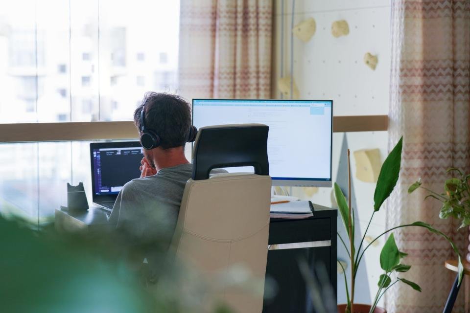 Vue arrière d'un homme dans un bureau moderne travaillant avec un ordinateur portable et un ordinateur de bureau.