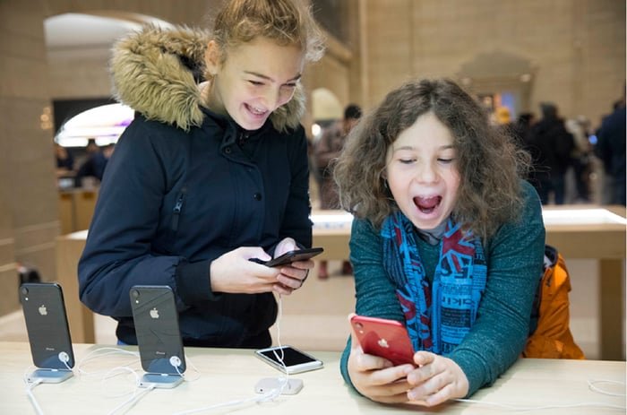 Deux enfants jubilatoires jouant avec des iPhones affichés dans un Apple Store.