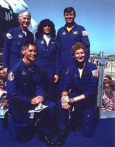 Cinq des six membres de l'équipage du STS-41D, Richard M. Mike Mullane, agenouillé à gauche, Steven A. Hawley, Henry W. Hank Hartsfield, debout à gauche, Judith A. Resnik et Michael L. Coats, posent avec Discovery en toile de fond.