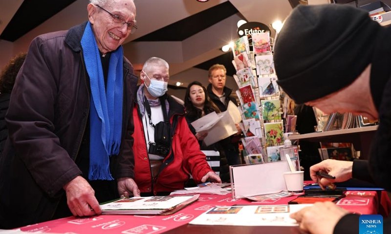 Chen Jianghong, un artiste français d'origine chinoise qui a conçu une paire de timbres pour célébrer le prochain Nouvel An lunaire chinois, signe pour un philatéliste à Paris, en France, le 26 janvier 2024. Le groupe français La Poste a dévoilé vendredi une paire de timbres. pour célébrer le prochain Nouvel An lunaire chinois, l'Année du Dragon.(Xinhua/Gao Jing)
