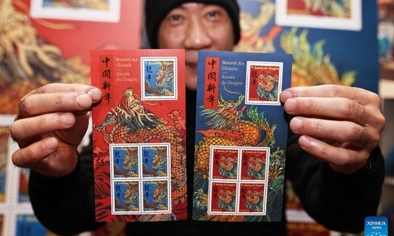 Chen Jianghong, un artiste français d'origine chinoise qui a conçu une paire de timbres pour célébrer le prochain Nouvel An lunaire chinois, signe pour un philatéliste à Paris, en France, le 26 janvier 2024. Le groupe français La Poste a dévoilé vendredi une paire de timbres. pour célébrer le prochain Nouvel An lunaire chinois, l'Année du Dragon.(Xinhua/Gao Jing)