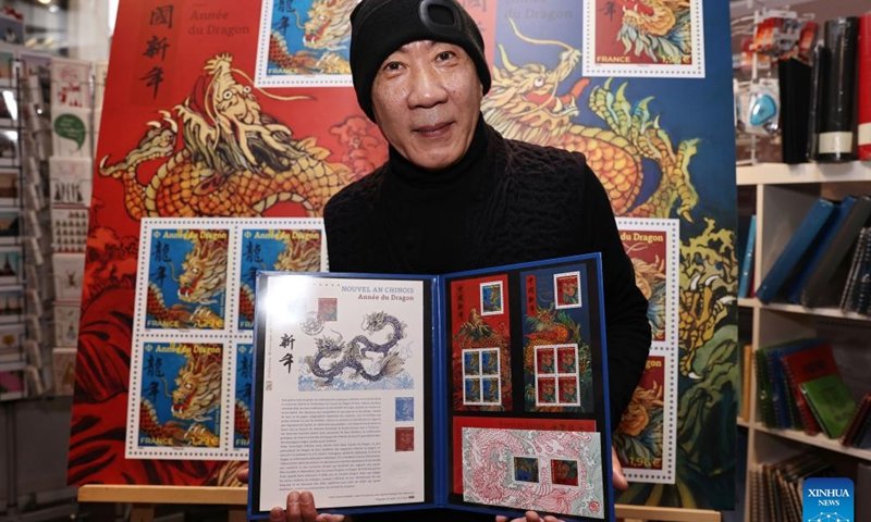 Chen Jianghong, un artiste français d'origine chinoise qui a conçu une paire de timbres pour célébrer le prochain Nouvel An lunaire chinois, signe pour un philatéliste à Paris, en France, le 26 janvier 2024. Le groupe français La Poste a dévoilé vendredi une paire de timbres. pour célébrer le prochain Nouvel An lunaire chinois, l'Année du Dragon.(Xinhua/Gao Jing)