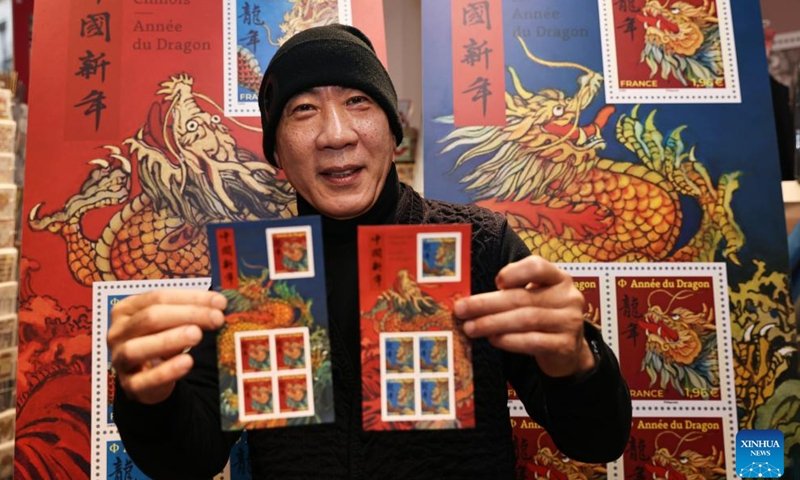 Chen Jianghong, un artiste français d'origine chinoise qui a conçu une paire de timbres pour célébrer le prochain Nouvel An lunaire chinois, signe pour un philatéliste à Paris, en France, le 26 janvier 2024. Le groupe français La Poste a dévoilé vendredi une paire de timbres. pour célébrer le prochain Nouvel An lunaire chinois, l'Année du Dragon.(Xinhua/Gao Jing)