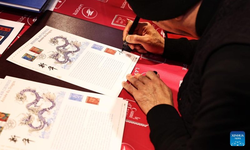 Chen Jianghong, un artiste français d'origine chinoise qui a conçu une paire de timbres pour célébrer le prochain Nouvel An lunaire chinois, signe pour un philatéliste à Paris, en France, le 26 janvier 2024. Le groupe français La Poste a dévoilé vendredi une paire de timbres. pour célébrer le prochain Nouvel An lunaire chinois, l'Année du Dragon.(Xinhua/Gao Jing)