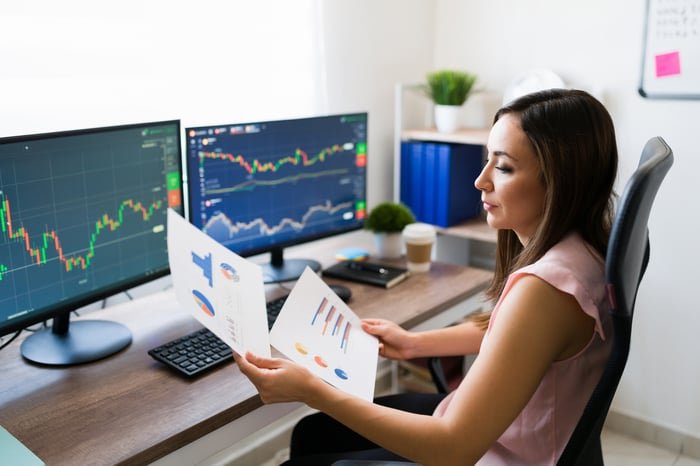 Une personne vérifie les graphiques financiers devant deux écrans de trading.