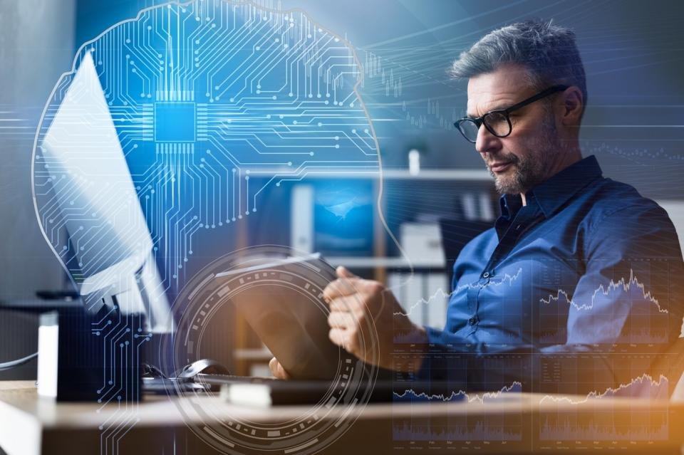 Une personne regardant un appareil mobile assise devant un bureau d'ordinateur avec une superposition d'algorithmes d'IA et de graphiques de cours boursiers.