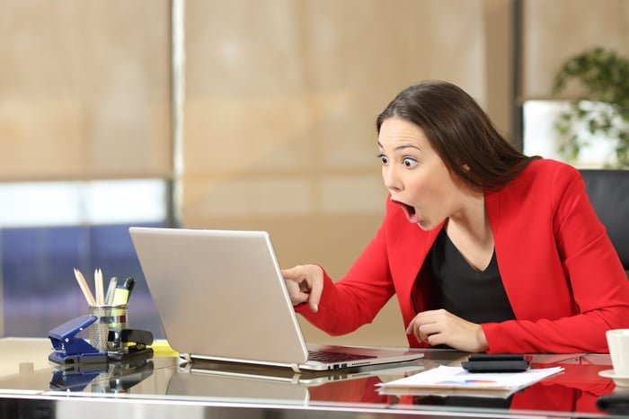 Un homme d'affaires haletant et pointant du doigt l'écran d'un ordinateur portable, visiblement choqué.