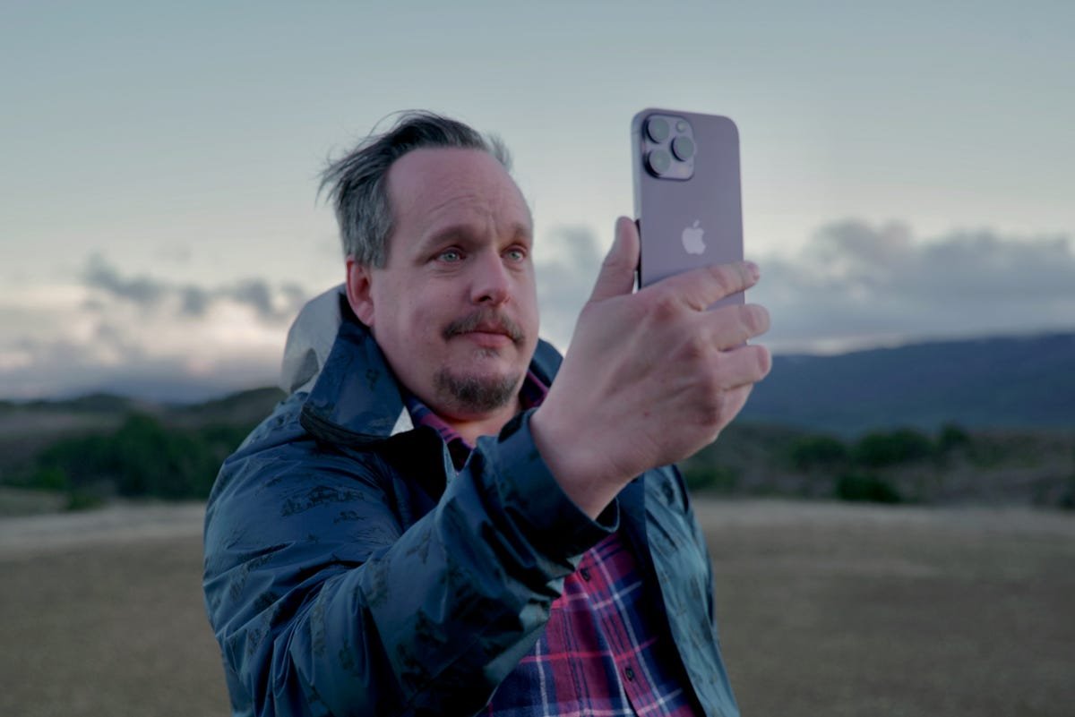 Un homme tenant un iPhone 14 Pro en plein air sur une colline isolée