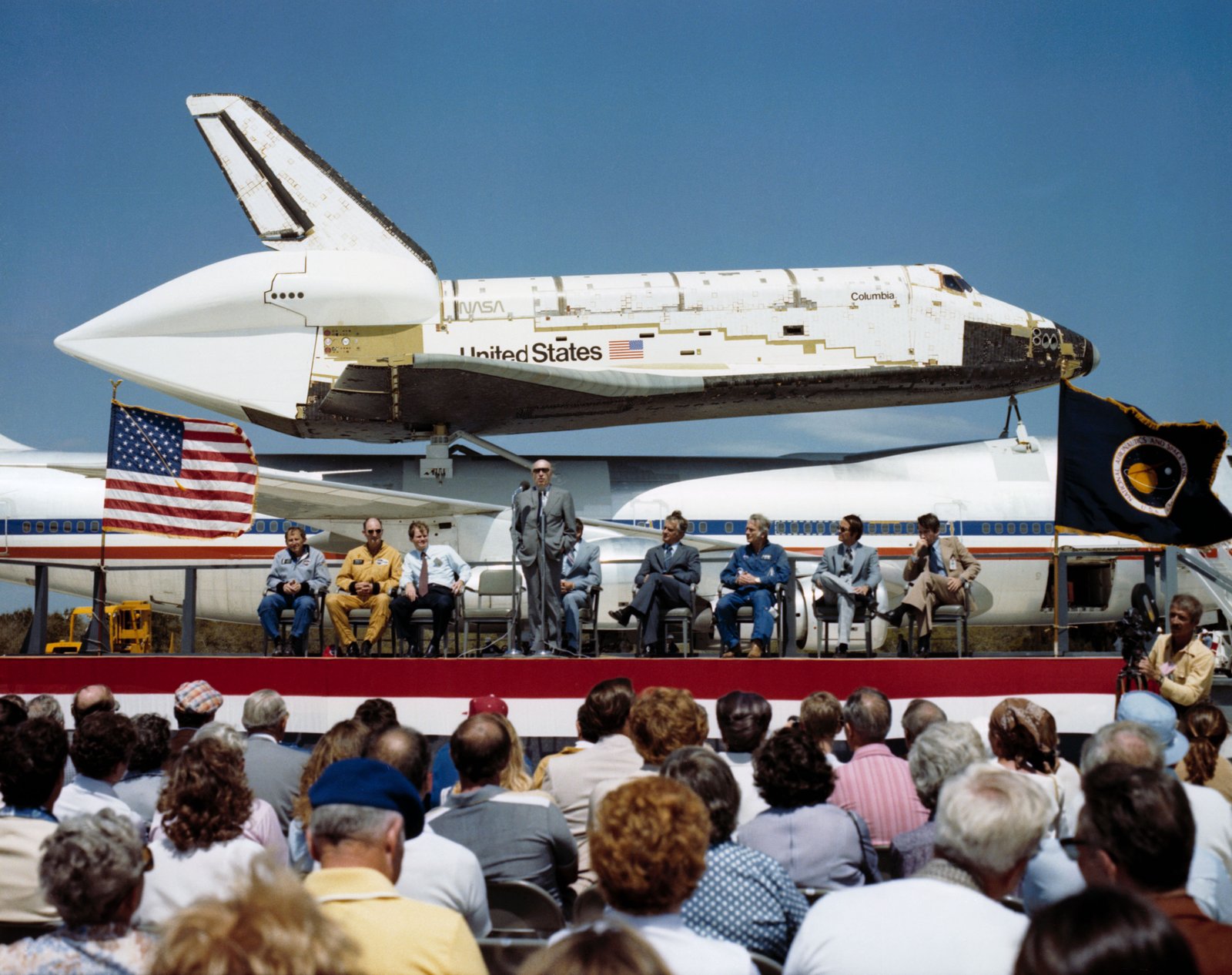 Au SLF, l'administrateur de la NASA, Robert A. Frosch, s'adresse à la foule rassemblée pour accueillir Columbia au KSC, tandis que d'autres dignitaires l'écoutent.