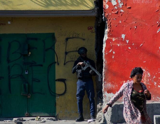Une femme passe devant un policier armé surveillant une rue après les violences des gangs dans le quartier dans la soirée du 21 mars 2024, à Port-au-Prince, en Haïti. 