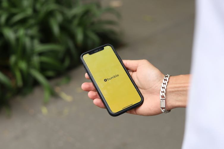 une main de femme tenant un téléphone affichant un fond jaune avec le mot BUMBLE