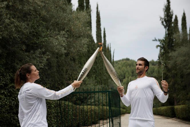 Le premier relayeur grec, le rameur Stefanos Ntouskos, allume la touche de la deuxième relayeuse, la nageuse française Laure Manaudou, lors du relais de la flamme après la cérémonie d'allumage de la flamme des Jeux olympiques de Paris 2024, le 16 avril 2024.