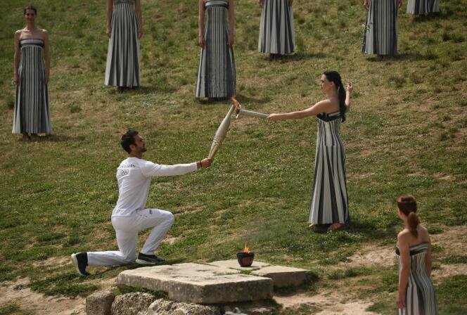 Premier porteur de la flamme, Stephanos Ntouskos (L) reçoit la flamme des mains de l'actrice grecque Mary Mina, alors qu'il commence sa course avec la flamme olympique après la cérémonie d'allumage de la flamme des Jeux Olympiques de Paris 2024 au lieu de naissance des Jeux olympiques antiques dans le sud de la Grèce, le 16 avril 2024.  