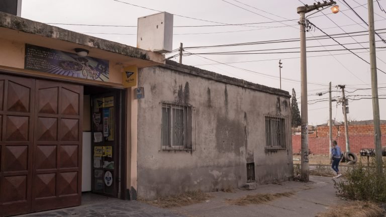 La crise économique en Argentine, une bénédiction déguisée pour les cybercafés 6 Une photo montrant l’extérieur d’un bâtiment avec un extérieur en béton gris et une porte rouge, tandis qu’une femme passe.