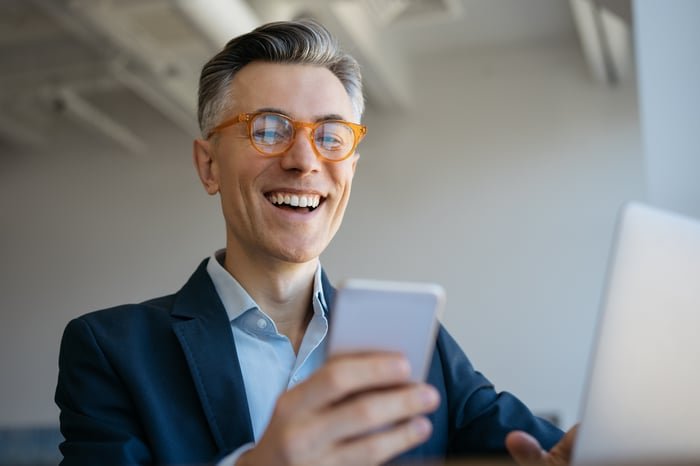Une personne souriante avec un ordinateur portable et un téléphone portable.