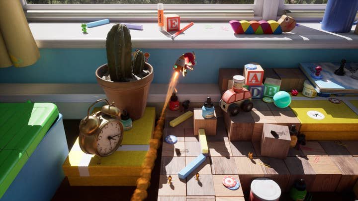 Capture d'écran de Plucky Squire montrant l'écuyer caricatural avec un sac à dos-fusée souriant survolant un bureau couvert de jouets et de blocs de construction, avec un vieux réveil et un cactus sur le côté