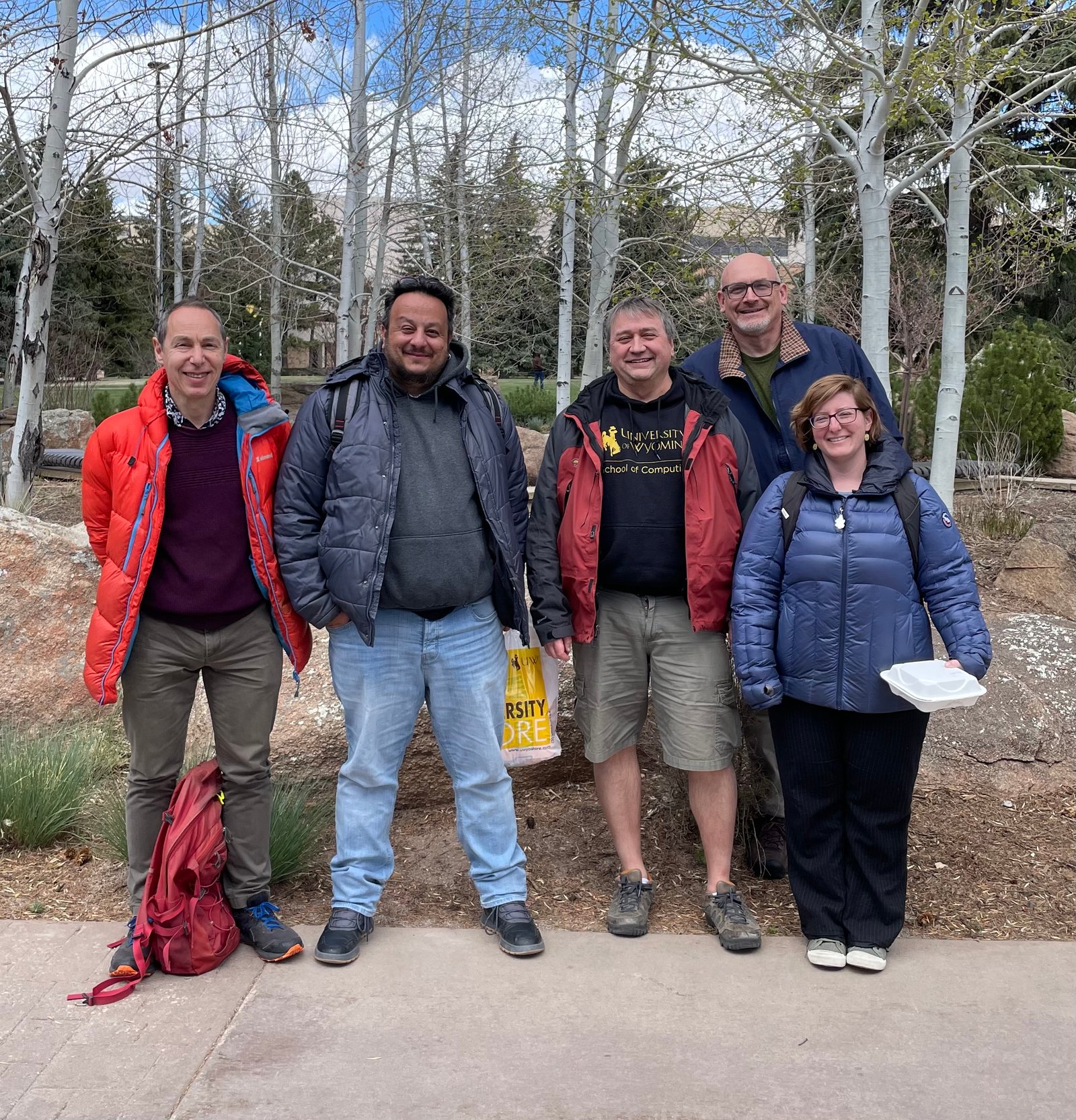 Cinq personnes debout ensemble avec plusieurs trembles sans feuilles derrière eux.