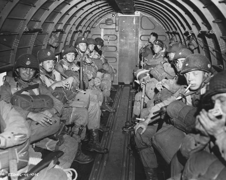 Fumant, bavardant, souriant ou simplement assis, plongés dans leurs pensées, des parachutistes américains, lourdement armés, survolent la Manche le 6 juin 1945. Ils joueront un rôle clé dans l'invasion de la Normandie en débarquant à l'intérieur des terres du front de 100 milles.  (Photo AP/Corps des transmissions des États-Unis)