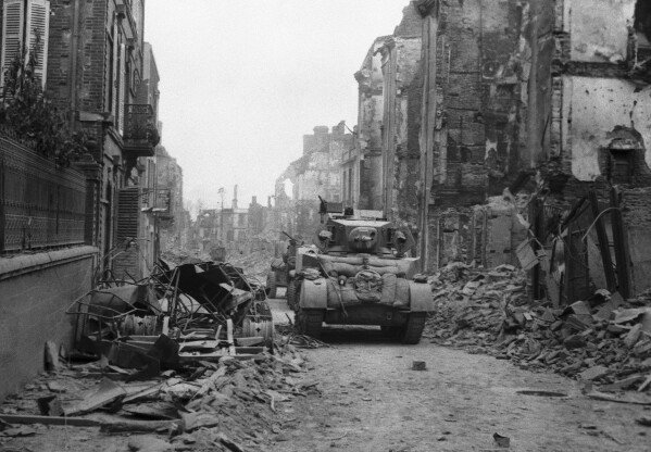 DOSSIER - Un char britannique avance dans une rue, alors que la bataille est toujours en cours, alors que la ville est toujours bordée de canons nazis qui lancent continuellement des obus dans la rue, à Saint-Lo, en Normandie, en France, le 20 juin 1944. (Photo AP, dossier)