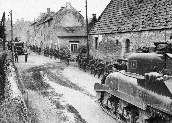 DOSSIER – Les troupes et véhicules britanniques traversant un village de Normandie sont occupés à poser des câbles de communication tandis que les blindés britanniques, canadiens et américains les font passer en route vers la ligne de front, le 13 juin 1944. (Photo AP, File)